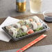 A sushi roll in a rectangular plastic container with a clear lid.
