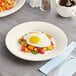 An Acopa ivory stoneware plate with a fried egg and vegetables on it.