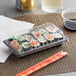 A rectangular plastic container of sushi with chopsticks on a table.