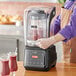 A person in an apron and gloves uses an AvaMix commercial blender to make a smoothie.