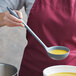 A woman using a Tablecraft gray flexible silicone ladle to serve soup.