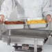 A chef holding a Choice stainless steel divided steam table pan full of food.