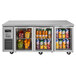 A Turbo Air undercounter refrigerator with glass doors full of fruit and drinks.