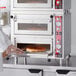 A person putting a pizza in an Avantco countertop pizza oven.