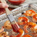A hand brushes Frank's RedHot Rajili sauce onto shrimp on a grill.