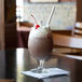 A white Aardvark paper straw in a glass of chocolate milkshake with a cherry on top.