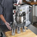 A man in a chef's uniform using the #5 Hub Meat Grinder and Pasta Roller / Cutter Attachment Kit on a mixer.