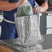 A person in a blue apron putting a bag of vegetables in a foil-lined box.