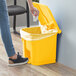 A woman's hand throws paper into a yellow Lavex rectangular step-on trash can.