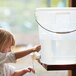 A young girl pouring water from a faucet into a large clear plastic round container.