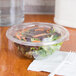 A salad in a Sabert clear plastic bowl with a fork on a napkin.