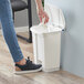 A person's hand putting a white bag in a Lavex white rectangular step-on trash can.