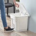 A woman using a white towel to clean a Lavex rectangular step-on trash can.