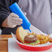 A person using a blue Choice wide mouth squeeze bottle to put mayonnaise on a burger.