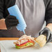 A person in black gloves using a Choice light blue plastic squeeze bottle to put sauce on a sandwich.