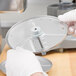 A person in white gloves uses a Robot Coupe 1/4" Julienne Cutting Disc to cut circular food.