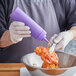 A person using a purple Choice wide mouth squeeze bottle to pour sauce onto food.