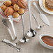 A table with Acopa stainless steel ladles, spoons, and a bowl of brown sauce.