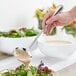 A hand holding an Acopa Edgeworth stainless steel ladle over a bowl of salad.