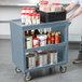 A man using a Cambro slate blue plastic utility cart to serve food and spices.