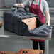 A woman holding a Vesture NextPhase black insulated pizza delivery bag full of pizza boxes.