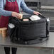 A person in a red apron putting food in a Vesture thermal bag.