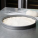 Pizza dough in an American Metalcraft hard coat anodized aluminum pizza pan on a counter.