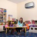 A woman sitting at a table with children around her uses a silver AeraMax PRO IV air purifier.