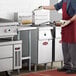 A man in a red apron using an Avantco electric floor fryer in a commercial kitchen.