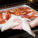 A person using a San Jamar terry cloth pan grabber to hold a tray of bacon.