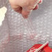 A person using a plastic glove to hold a red Lavex insulated delivery bag.