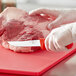 A person in white gloves using a Choice serrated utility knife with a red handle to cut meat.