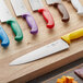 A yellow Choice chef knife on a cutting board with other colored Choice chef knives.