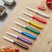 A group of Choice paring knives with colorful handles on a cutting board.