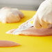 A person using a Choice smooth edge paring knife with a neon yellow handle to cut chicken on a yellow cutting board.