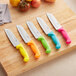 A group of Choice Santoku knives with colorful handles on a cutting board.