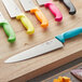 A Choice 10" chef knife with a neon orange handle on a wooden surface.