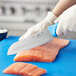 A person's hand using a Choice Santoku knife with a blue handle to cut salmon.