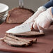 A person using a Choice 6" Chef Knife with a brown handle to cut meat on a cutting board.