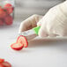 A person in gloves uses a Choice smooth edge paring knife to cut a strawberry.