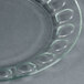 A close up of an Arcoroc clear glass dinner plate with a circular design.