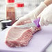 A person in a professional kitchen using a Choice curved stiff boning knife with a purple handle to cut meat.