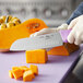 A person holding a Choice 7" Santoku Knife with a purple handle cutting a butternut squash.