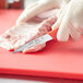 A person using a Choice smooth edge paring knife with a red handle to cut raw meat on a red cutting board.