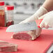 A person using a Choice Santoku knife with a red handle to cut meat.