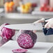 A person cutting a red cabbage with a Choice 12" Chef Knife.