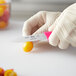 A person in gloves uses a Choice neon pink serrated edge paring knife to cut a yellow tomato.