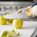A person cutting a yellow apple with a Choice 8" Chef Knife with a neon orange handle.