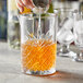 A person pouring an orange drink from a glass pitcher into a Pasabahce Timeless Vintage stirring glass.