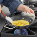 A person uses a Vigor SS1 stainless steel fry pan with dual handles to cook an omelette on a stove.